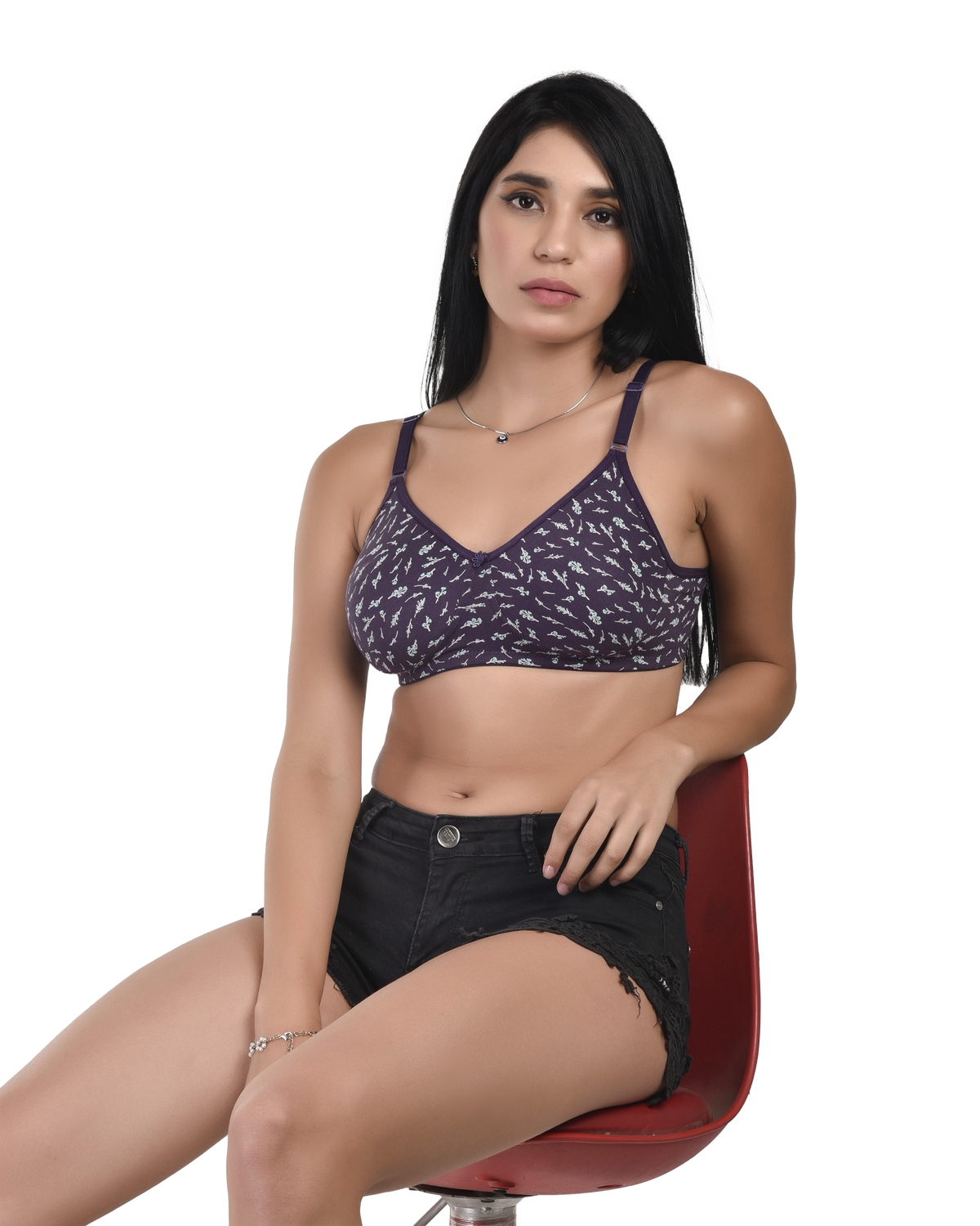 Woman wearing a patterned top and black shorts sitting on a red chair against a white background