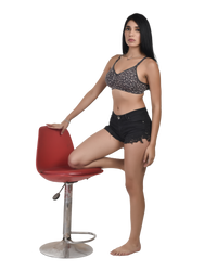 Woman in black patterned top and black shorts sitting on a red chair against a white background